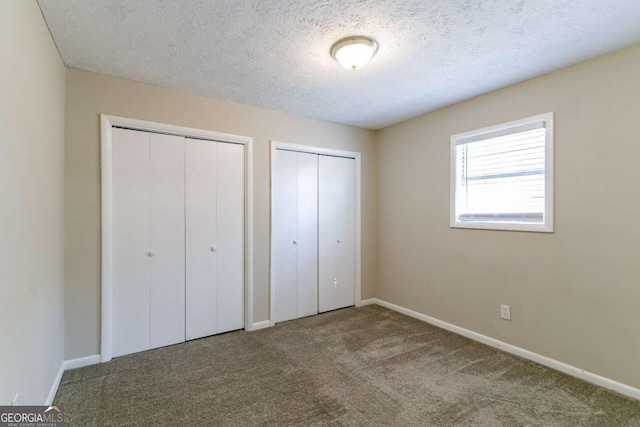 unfurnished bedroom with a textured ceiling, carpet, and two closets