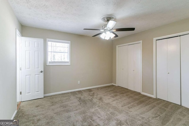 unfurnished bedroom with light carpet, a textured ceiling, two closets, and ceiling fan