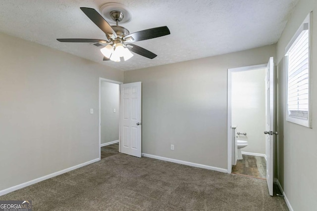 unfurnished bedroom featuring ceiling fan, dark carpet, ensuite bathroom, and a textured ceiling