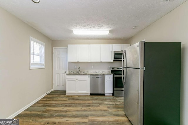 8775 Lee Rd, Lithia Springs, GA 30122 - kitchen featuring appliances with stainless steel finishes, white cabinets, wood finished floors, light stone countertops, and a textured ceiling