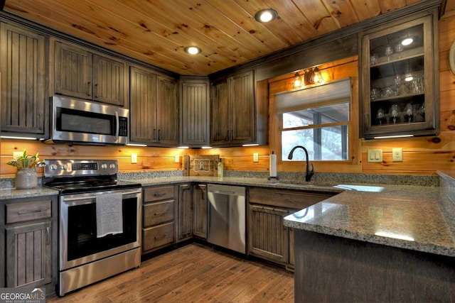 kitchen featuring dark stone counters, dark brown cabinetry, appliances with stainless steel finishes, and light hardwood / wood-style flooring