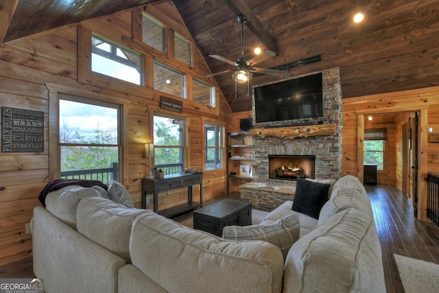 living room featuring dark hardwood / wood-style flooring, high vaulted ceiling, a stone fireplace, and a wealth of natural light