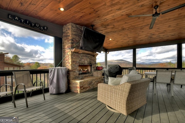 wooden terrace with an outdoor stone fireplace and ceiling fan