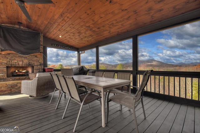 sunroom / solarium featuring an outdoor stone fireplace, vaulted ceiling, ceiling fan, wooden ceiling, and a mountain view