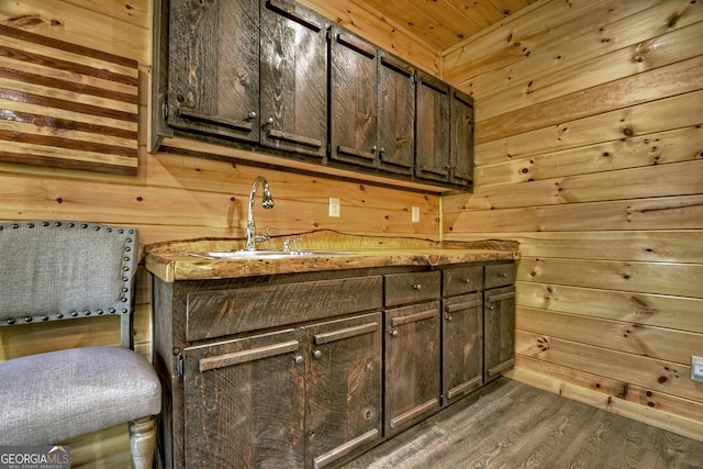 bar featuring dark brown cabinetry, dark hardwood / wood-style floors, wooden walls, and sink