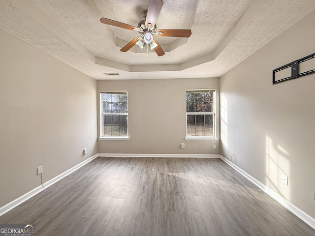 empty room with a textured ceiling, ceiling fan, a raised ceiling, and dark wood-type flooring