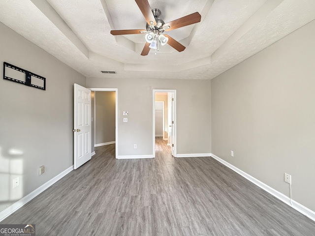 unfurnished bedroom featuring wood-type flooring, a textured ceiling, a raised ceiling, and ceiling fan