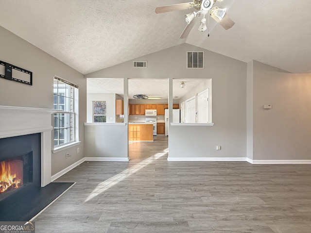 unfurnished living room featuring wood-type flooring, a textured ceiling, vaulted ceiling, and ceiling fan