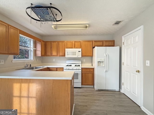 kitchen with a textured ceiling, white appliances, kitchen peninsula, and light hardwood / wood-style flooring