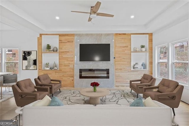 living room featuring plenty of natural light, wood walls, a fireplace, and ceiling fan