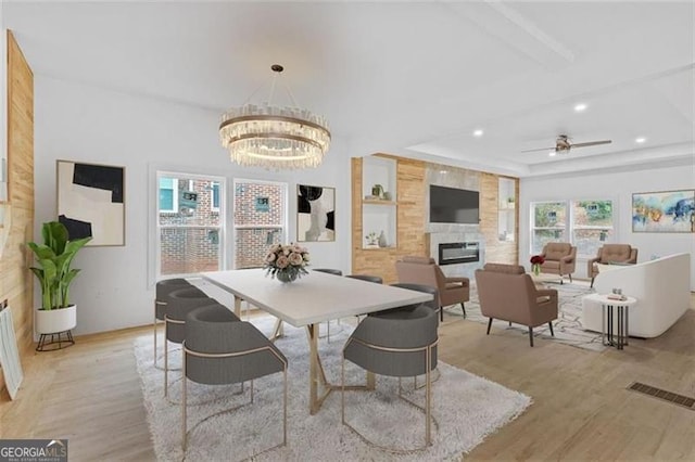 dining space featuring ceiling fan with notable chandelier, a fireplace, light hardwood / wood-style flooring, and a tray ceiling