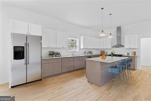 kitchen featuring stainless steel refrigerator with ice dispenser, a center island, light hardwood / wood-style flooring, and wall chimney exhaust hood