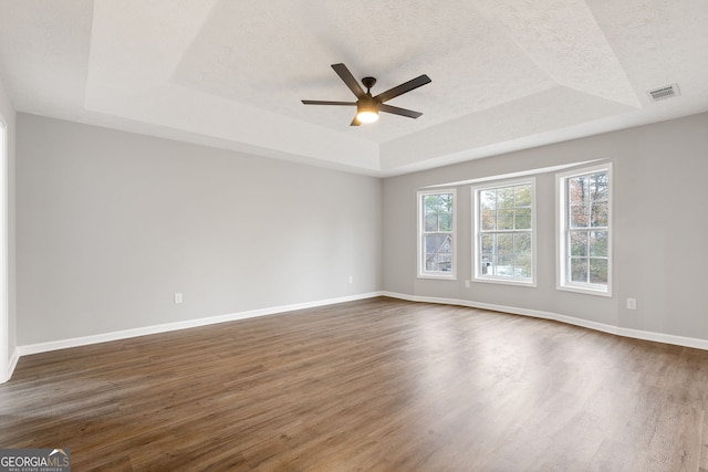 empty room featuring a textured ceiling, ceiling fan, a raised ceiling, and dark wood-type flooring