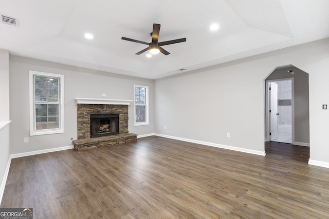 unfurnished living room featuring a raised ceiling, a fireplace, ceiling fan, and dark hardwood / wood-style flooring