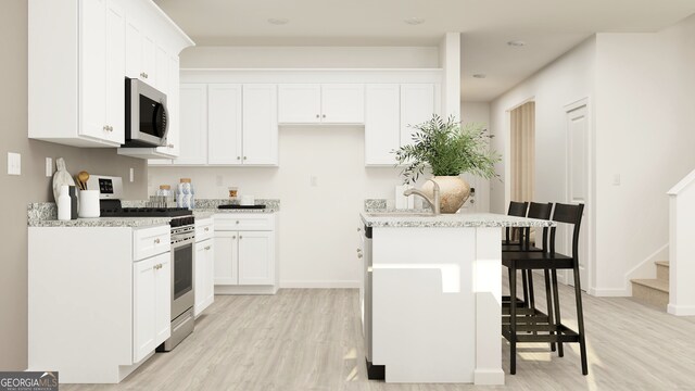 kitchen featuring a kitchen breakfast bar, light hardwood / wood-style flooring, a center island with sink, white cabinets, and appliances with stainless steel finishes