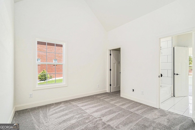 unfurnished bedroom featuring ensuite bathroom, light colored carpet, and high vaulted ceiling