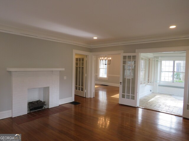 unfurnished living room featuring dark hardwood / wood-style floors, ornamental molding, a chandelier, and a brick fireplace