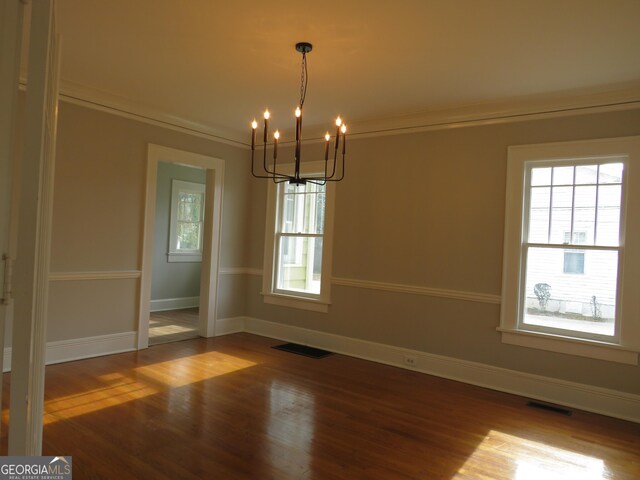 unfurnished dining area with hardwood / wood-style flooring, crown molding, and an inviting chandelier