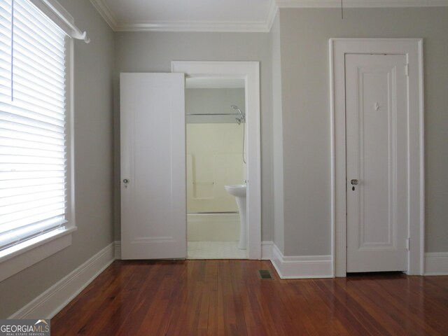 unfurnished bedroom with ensuite bath, multiple windows, dark wood-type flooring, and crown molding