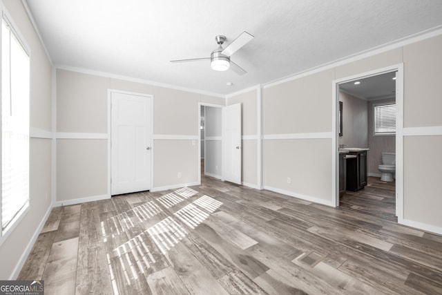 unfurnished bedroom featuring ensuite bath, ornamental molding, ceiling fan, hardwood / wood-style flooring, and a closet