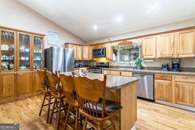 kitchen with appliances with stainless steel finishes, a breakfast bar area, light wood-type flooring, and lofted ceiling