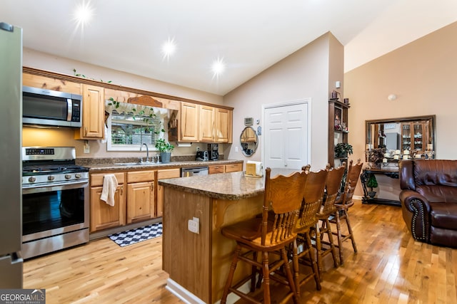 kitchen featuring a breakfast bar, a sink, a center island, appliances with stainless steel finishes, and vaulted ceiling