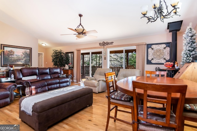 living room with ceiling fan with notable chandelier, light wood-style floors, and vaulted ceiling