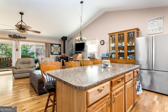 kitchen with light wood finished floors, a wood stove, freestanding refrigerator, a kitchen bar, and open floor plan