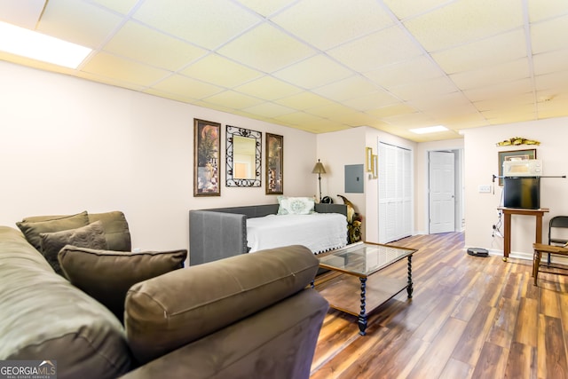 living room featuring wood finished floors, electric panel, a paneled ceiling, and baseboards