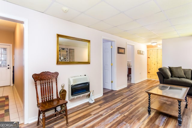 living room featuring heating unit, a paneled ceiling, baseboards, and wood finished floors