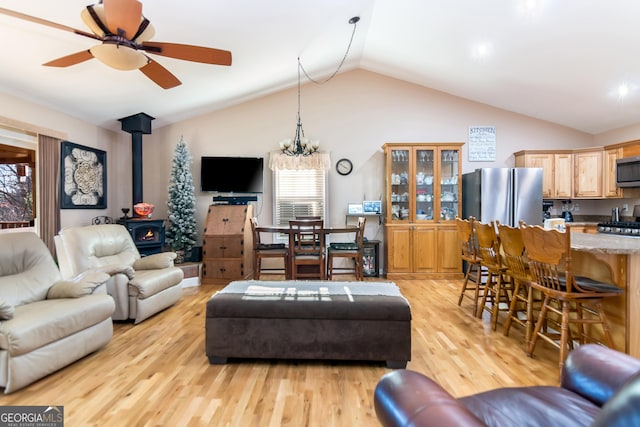 living area featuring lofted ceiling, a ceiling fan, a wood stove, and light wood-style floors