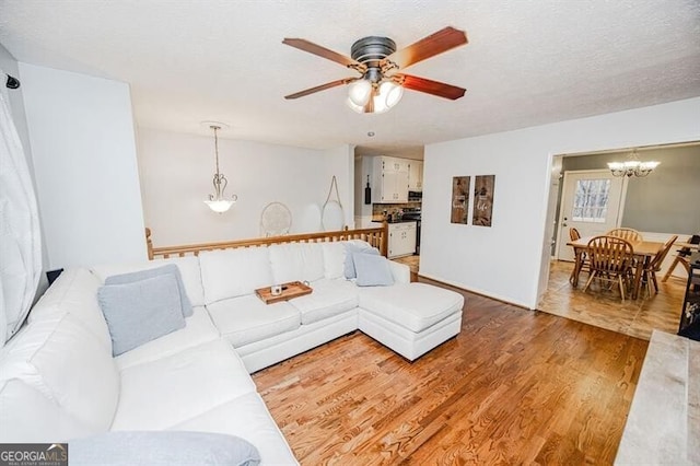 living room with ceiling fan with notable chandelier, wood-type flooring, and a textured ceiling