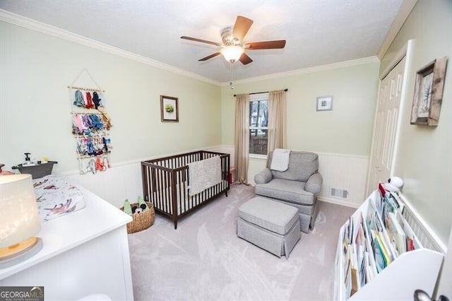 bedroom with crown molding, ceiling fan, a nursery area, light colored carpet, and a closet