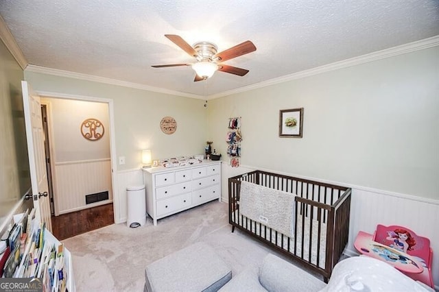 carpeted bedroom with ornamental molding, a nursery area, a textured ceiling, and ceiling fan