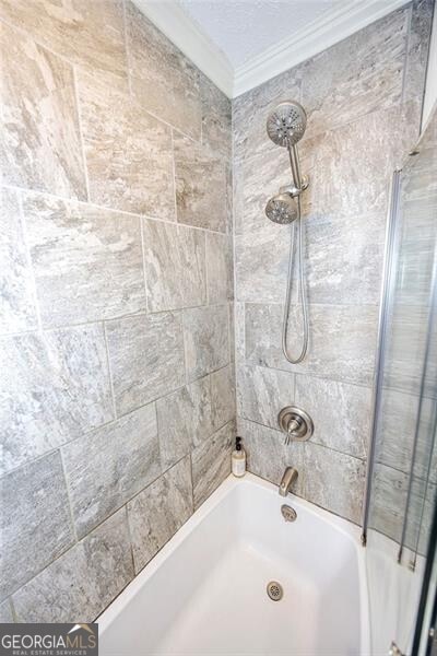 bathroom with crown molding and tiled shower / bath