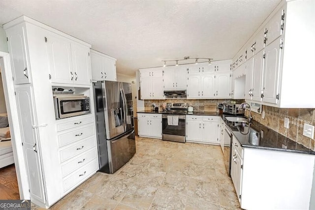 kitchen featuring sink, range hood, stainless steel appliances, white cabinets, and dark stone counters