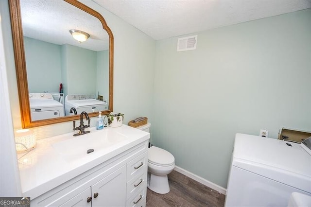 bathroom featuring toilet, a textured ceiling, vanity, hardwood / wood-style floors, and washing machine and dryer