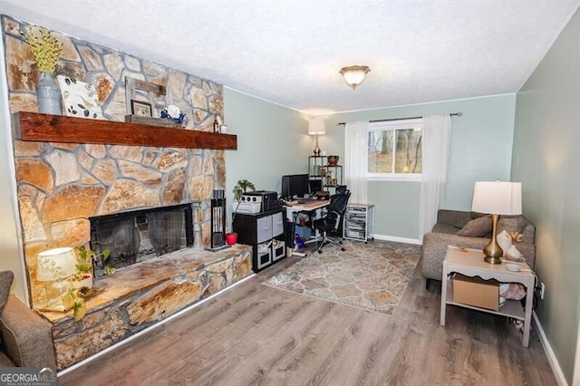 home office with hardwood / wood-style flooring, a stone fireplace, and a textured ceiling