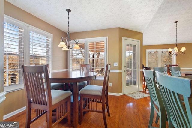 dining space with wood-type flooring, a notable chandelier, and a textured ceiling