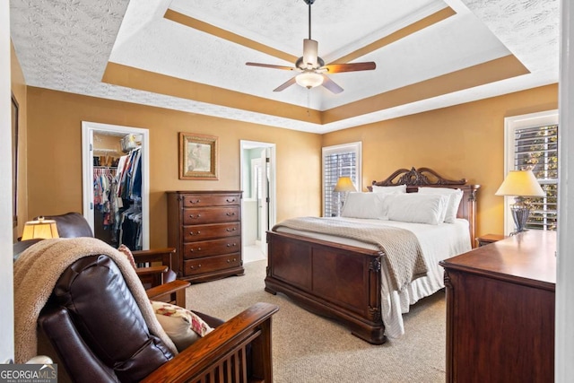 carpeted bedroom with a tray ceiling, a textured ceiling, ceiling fan, and a spacious closet