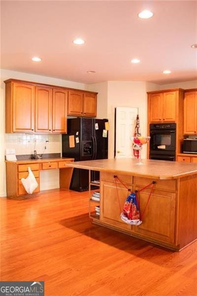 kitchen featuring light wood-type flooring, backsplash, and black appliances