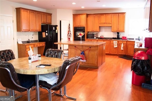 kitchen with decorative backsplash, a breakfast bar, black appliances, a center island with sink, and light wood-type flooring