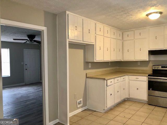 kitchen with stainless steel electric stove, ceiling fan, white cabinets, and a textured ceiling