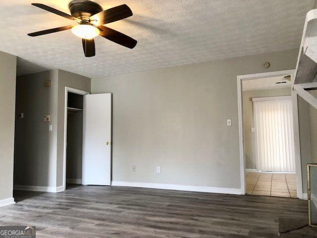 empty room with ceiling fan, wood-type flooring, and a textured ceiling