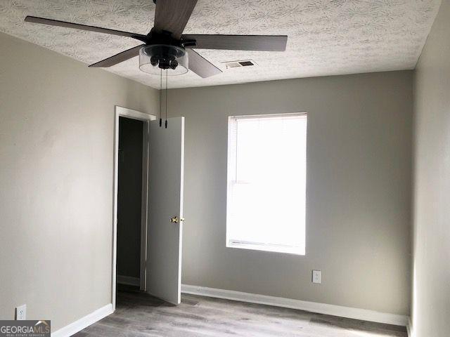 unfurnished bedroom with multiple windows, ceiling fan, wood-type flooring, and a textured ceiling