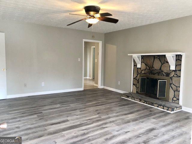 unfurnished living room with ceiling fan, a fireplace, a textured ceiling, and hardwood / wood-style flooring