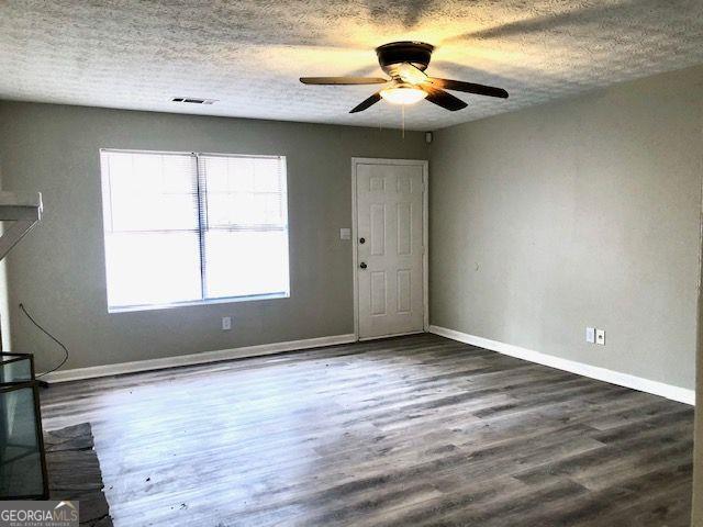 unfurnished room with a textured ceiling, ceiling fan, and dark wood-type flooring