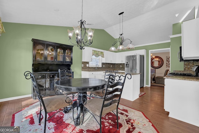 dining room featuring a notable chandelier, dark hardwood / wood-style flooring, sink, and vaulted ceiling