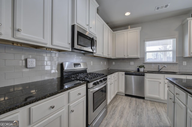 kitchen with stainless steel appliances, sink, dark stone countertops, and white cabinets