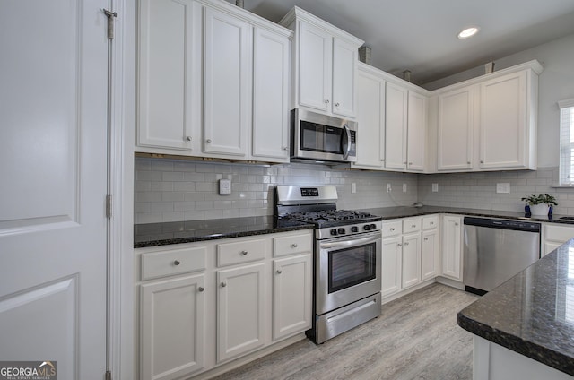 kitchen with light wood-type flooring, dark stone counters, stainless steel appliances, decorative backsplash, and white cabinets